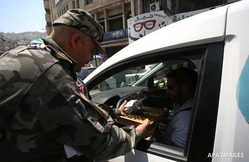 A Palestinian security man distributes sweets to people in the street, as a celebration of the victory at Al-Aqsa Mosque, in the West Bank City of Hebron, on July 27, 2017. Israel removed security apparatus from the entr...