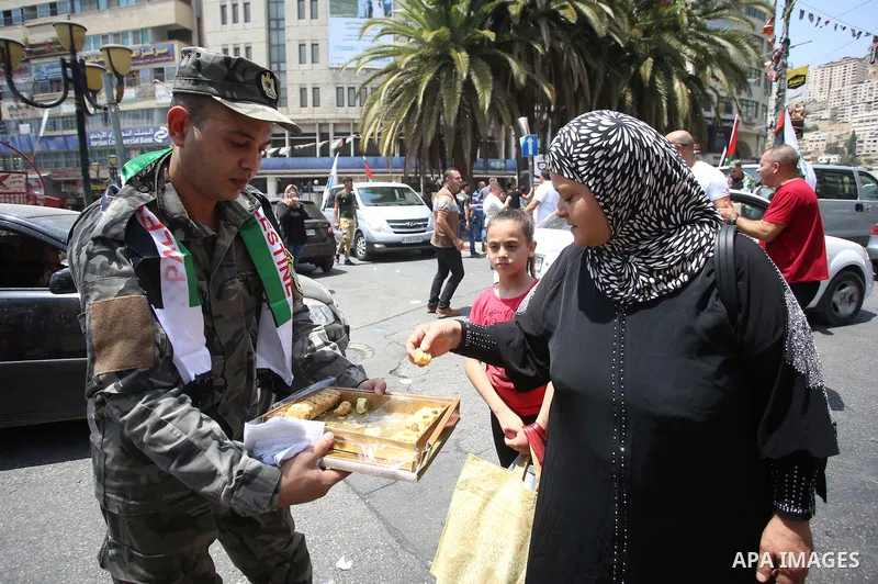A Palestinian security man distributes sweets to people in the street, as a celebration of the victory at Al-Aqsa Mosque, in the West Bank City of Hebron, on July 27, 2017. Israel removed security apparatus from the entr...