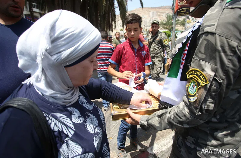 A Palestinian security man distributes sweets to people in the street, as a celebration of the victory at Al-Aqsa Mosque, in the West Bank City of Hebron, on July 27, 2017. Israel removed security apparatus from the entr...