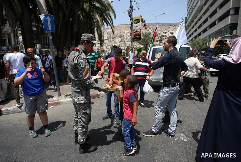 A Palestinian security man distributes sweets to people in the street, as a celebration of the victory at Al-Aqsa Mosque, in the West Bank City of Hebron, on July 27, 2017. Israel removed security apparatus from the entr...