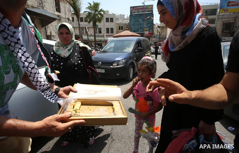A Palestinian man distributes sweets to people in the street, as a celebration of the victory at Al-Aqsa Mosque, in the West Bank City of Hebron, on July 27, 2017. Israel removed security apparatus from the entrance to t...