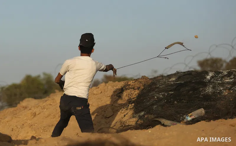 A Palestinian protester uses a slingshot to hurl stones towards Israeli security forces during clashes near the border between Israel and Central Gaza Strip July 28, 2017. Israeli troops shot dead a Palestinian teenager...