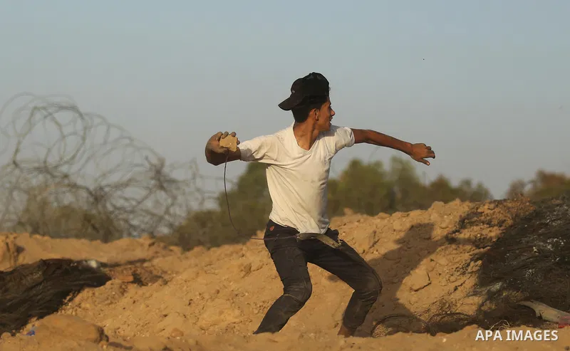 A Palestinian protester uses a slingshot to hurl stones towards Israeli security forces during clashes near the border between Israel and Central Gaza Strip July 28, 2017. Israeli troops shot dead a Palestinian teenager...