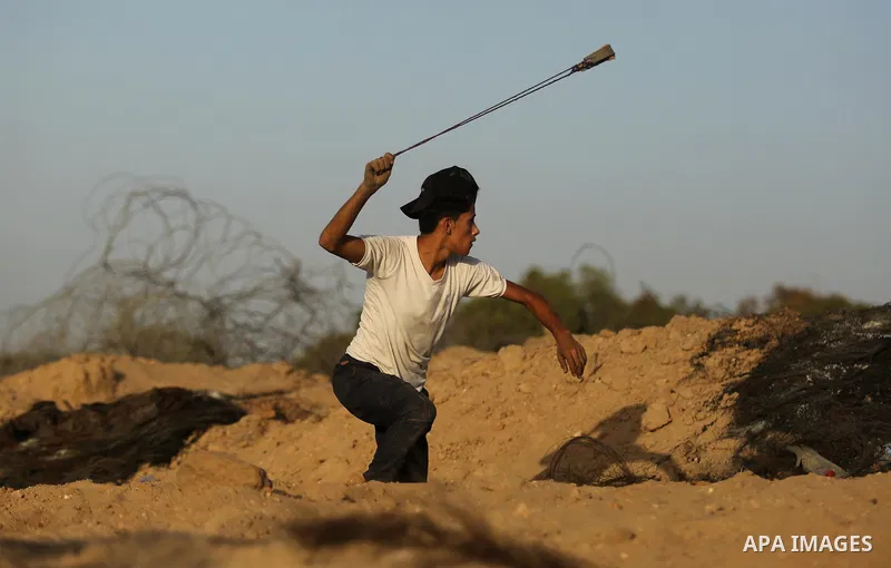 A Palestinian protester uses a slingshot to hurl stones towards Israeli security forces during clashes near the border between Israel and Central Gaza Strip July 28, 2017. Israeli troops shot dead a Palestinian teenager...