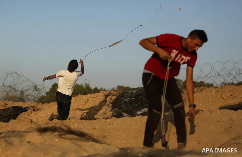 A Palestinian protester uses a slingshot to hurl stones towards Israeli security forces during clashes near the border between Israel and Central Gaza Strip July 28, 2017. Israeli troops shot dead a Palestinian teenager...
