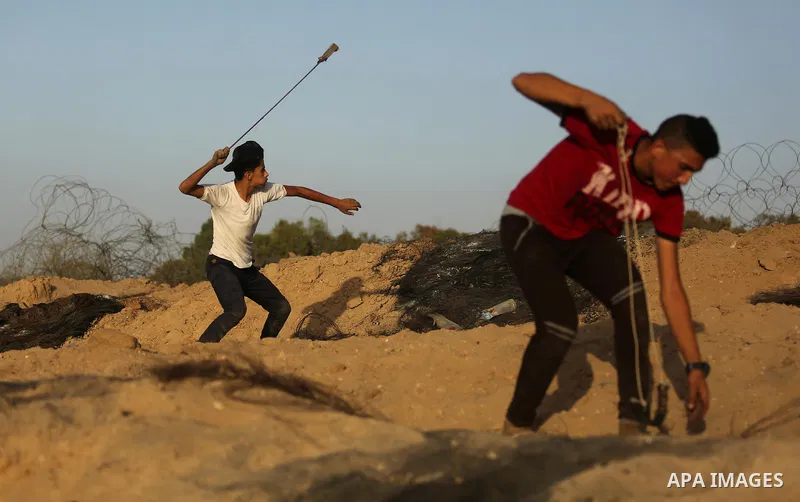 A Palestinian protester uses a slingshot to hurl stones towards Israeli security forces during clashes near the border between Israel and Central Gaza Strip July 28, 2017. Israeli troops shot dead a Palestinian teenager...
