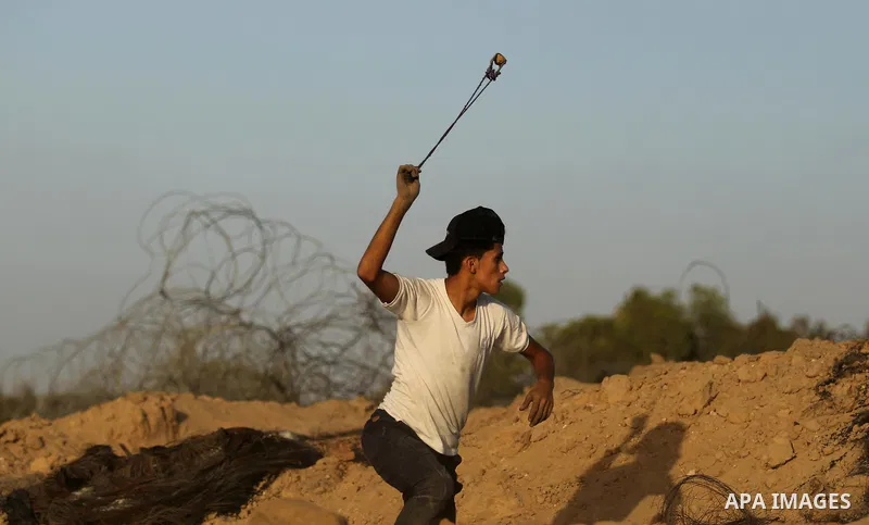 A Palestinian protester uses a slingshot to hurl stones towards Israeli security forces during clashes near the border between Israel and Central Gaza Strip July 28, 2017. Israeli troops shot dead a Palestinian teenager...
