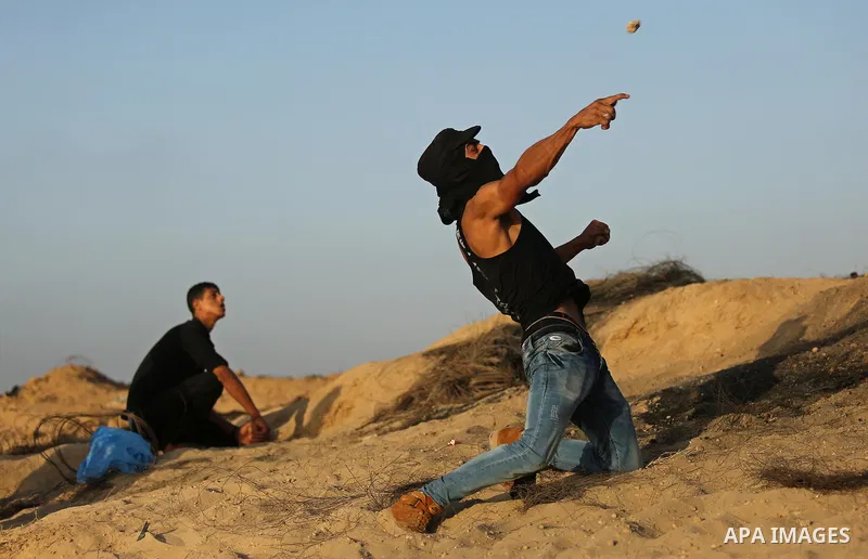 A Palestinian protester uses a slingshot to hurl stones towards Israeli security forces during clashes near the border between Israel and Central Gaza Strip July 28, 2017. Israeli troops shot dead a Palestinian teenager...