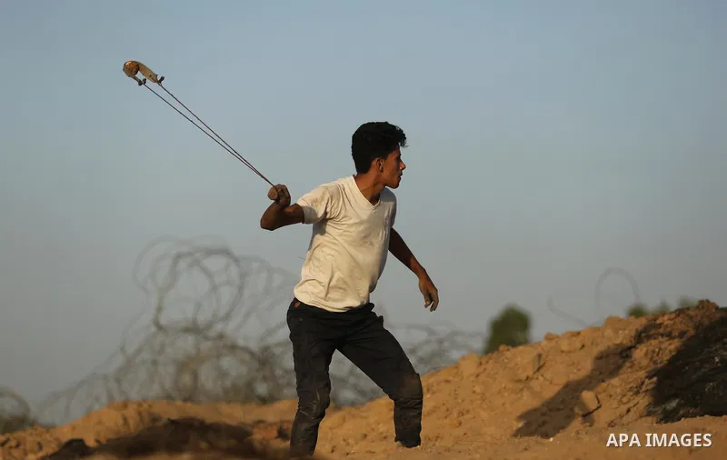 A Palestinian protester uses a slingshot to hurl stones towards Israeli security forces during clashes near the border between Israel and Central Gaza Strip July 28, 2017. Israeli troops shot dead a Palestinian teenager...