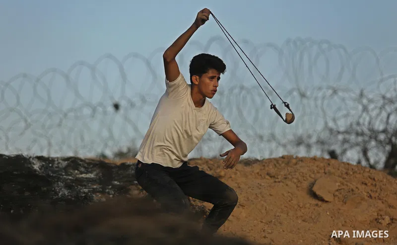 A Palestinian protester uses a slingshot to hurl stones towards Israeli security forces during clashes near the border between Israel and Central Gaza Strip July 28, 2017. Israeli troops shot dead a Palestinian teenager...