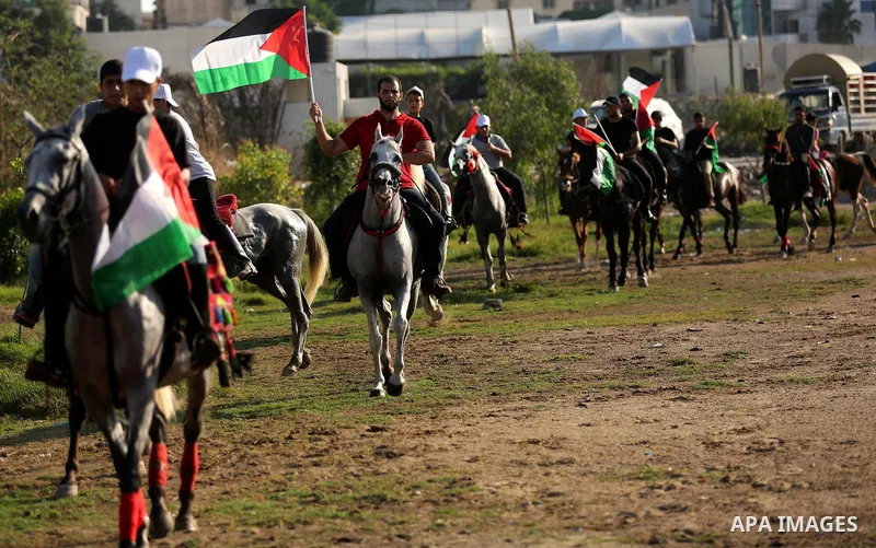 Palestinians hold the national flags as they ride horses during parade of horses in Gaza city on August 2, 2017. Photo by Ashraf Amra