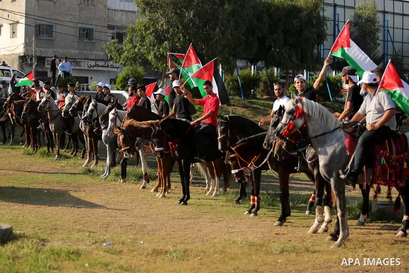 Palestinians hold the national flags as they ride horses during parade of horses in Gaza city on August 2, 2017. Photo by Ashraf Amra