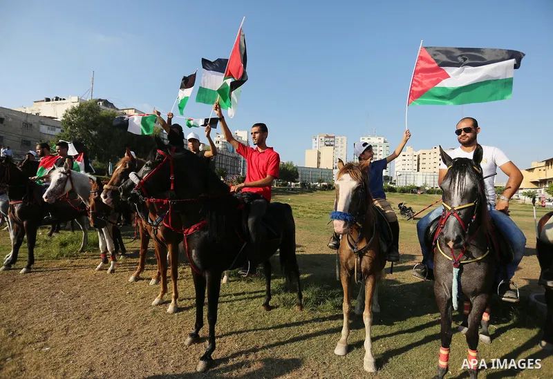 Palestinians hold the national flags as they ride horses during parade of horses in Gaza city on August 2, 2017. Photo by Ashraf Amra