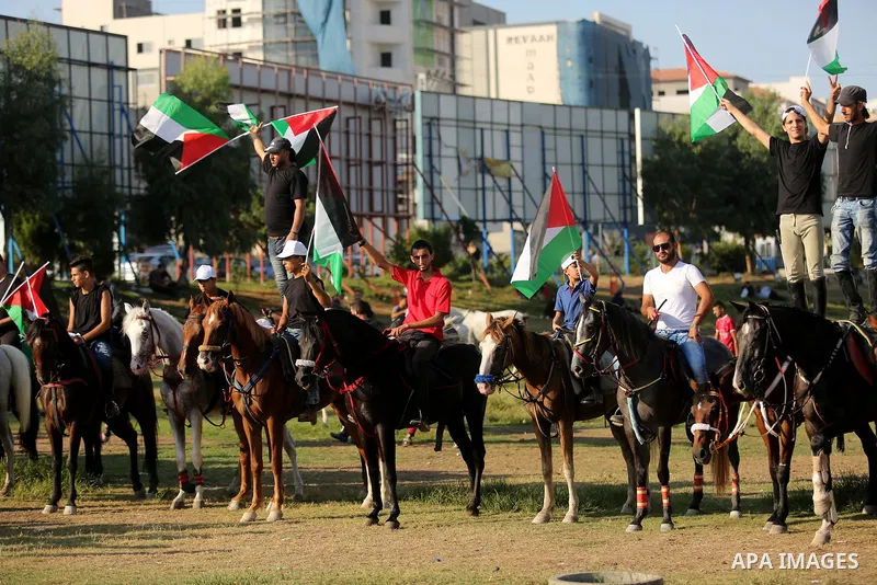 Palestinians hold the national flags as they ride horses during parade of horses in Gaza city on August 2, 2017. Photo by Ashraf Amra