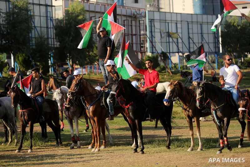 Palestinians hold the national flags as they ride horses during parade of horses in Gaza city on August 2, 2017. Photo by Ashraf Amra