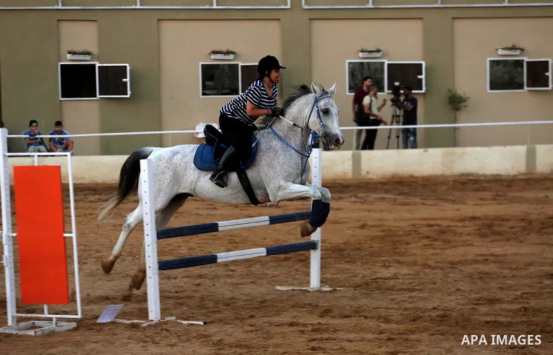 A Palestinian girl rides her horse during a jump obstacles championship, in Gaza city on August 4, 2017. Photo by Mohammed Asad
