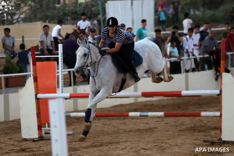 A Palestinian girl rides her horse during a jump obstacles championship, in Gaza city on August 4, 2017. Photo by Mohammed Asad