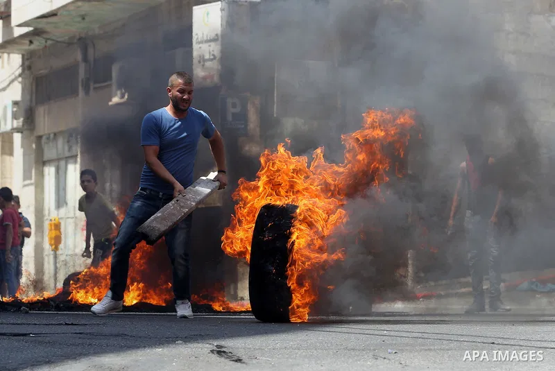Palestinian protesters burn a tyre during clashes between demonstrators and security forces in the city of Hebron in the Israeli-occupied West Bank, on July 28, 2017, as protests erupt in support of the Al-Aqsa mosque co...