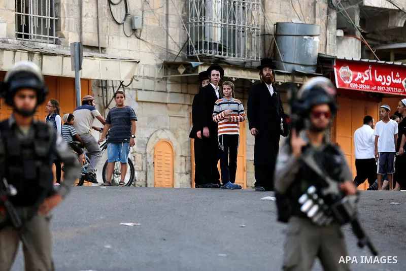 Israeli soldier stand guard while Ultra-Orthodox Jewish men under the protection of the soldiers visit a sacred Jewish site in the occupied West Bank city of Hebron, 01 August 2017. Photo by Wisam Hashlamoun