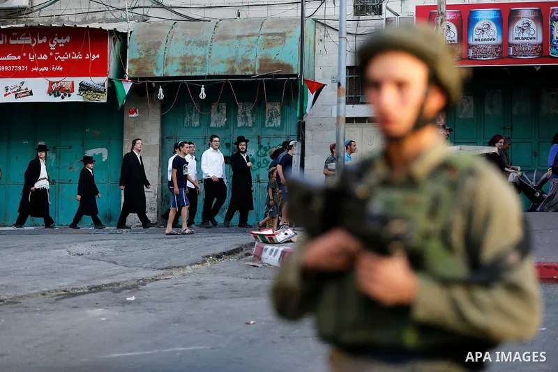 Israeli soldier stand guard while Ultra-Orthodox Jewish men under the protection of the soldiers visit a sacred Jewish site in the occupied West Bank city of Hebron, 01 August 2017. Photo by Wisam Hashlamoun