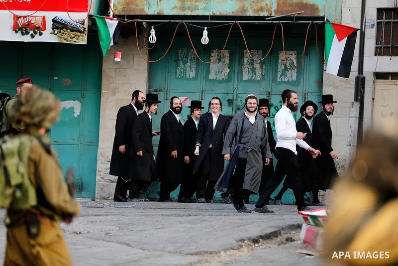 Israeli soldier stand guard while Ultra-Orthodox Jewish men under the protection of the soldiers visit a sacred Jewish site in the occupied West Bank city of Hebron, 01 August 2017. Photo by Wisam Hashlamoun