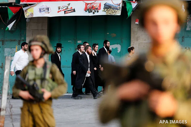Israeli soldier stand guard while Ultra-Orthodox Jewish men under the protection of the soldiers visit a sacred Jewish site in the occupied West Bank city of Hebron, 01 August 2017. Photo by Wisam Hashlamoun