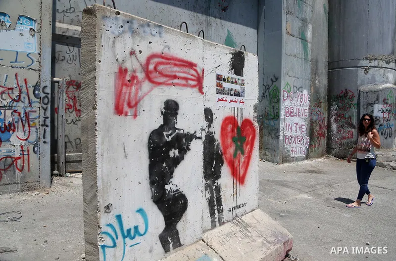 A tourist walks past a graffiti on the controversial Israeli separation barrier in the West Bank town of Bethlehem on August 8, 2017. Photo by Shadi Hatem