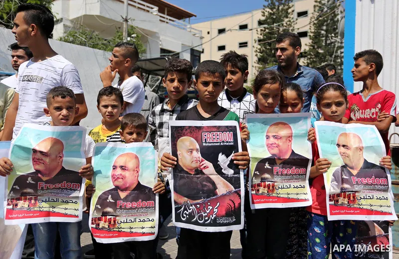 Palestinians hold posters of Mohammad El Halabi, World Vision's manager of operations in Gaza who was accused by Israel of funnelling millions of dollars in aid money to Hamas, during a protest in solidarity with El Hala...