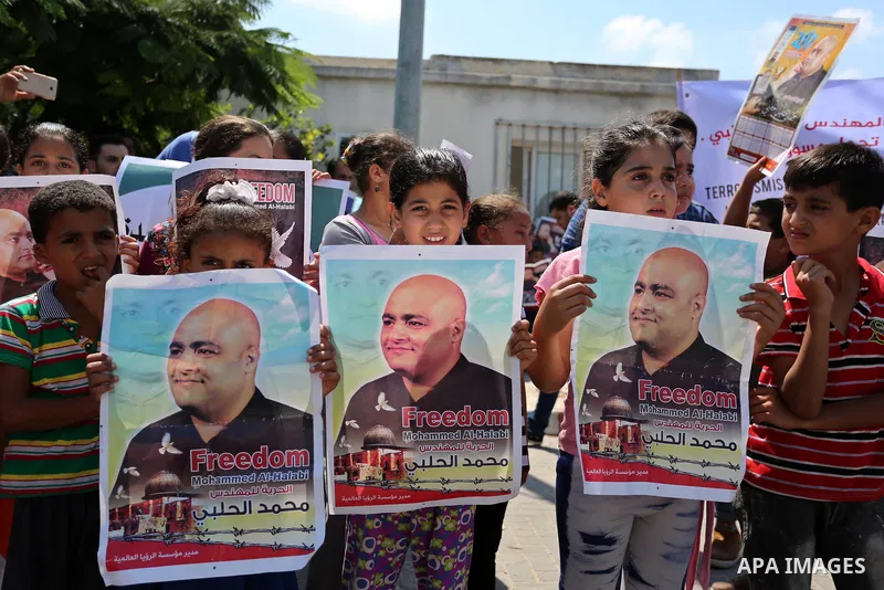 Palestinians hold posters of Mohammad El Halabi, World Vision's manager of operations in Gaza who was accused by Israel of funnelling millions of dollars in aid money to Hamas, during a protest in solidarity with El Hala...