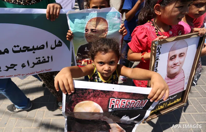 Palestinians hold posters of Mohammad El Halabi, World Vision's manager of operations in Gaza who was accused by Israel of funnelling millions of dollars in aid money to Hamas, during a protest in solidarity with El Hala...