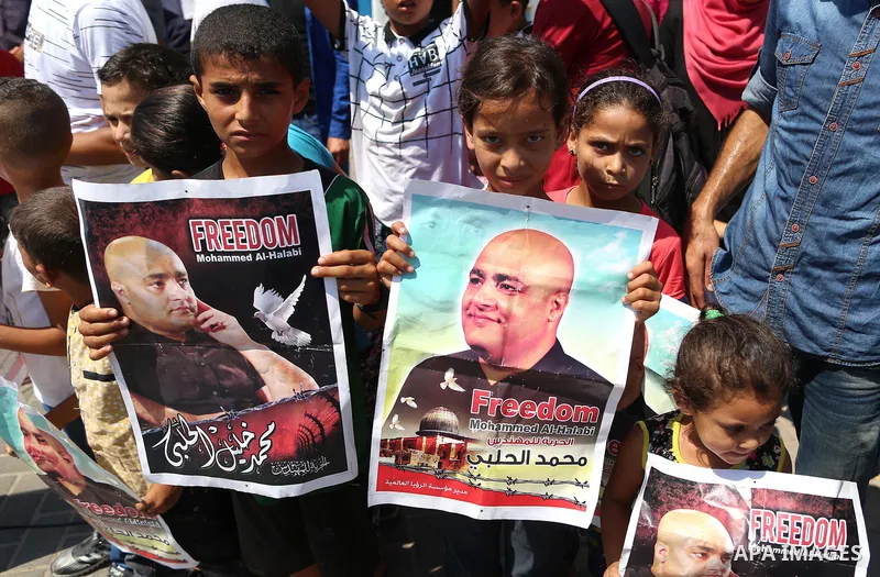 Palestinians hold posters of Mohammad El Halabi, World Vision's manager of operations in Gaza who was accused by Israel of funnelling millions of dollars in aid money to Hamas, during a protest in solidarity with El Hala...