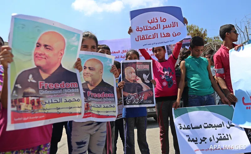 Palestinians hold posters of Mohammad El Halabi, World Vision's manager of operations in Gaza who was accused by Israel of funnelling millions of dollars in aid money to Hamas, during a protest in solidarity with El Hala...