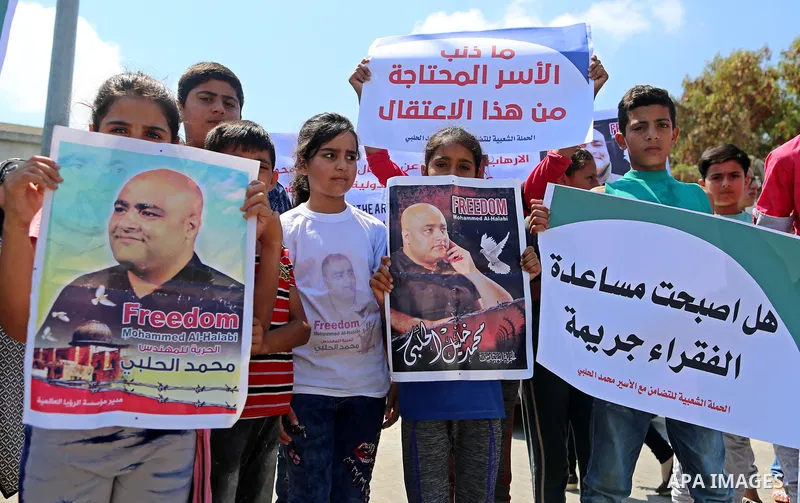 Palestinians hold posters of Mohammad El Halabi, World Vision's manager of operations in Gaza who was accused by Israel of funnelling millions of dollars in aid money to Hamas, during a protest in solidarity with El Hala...