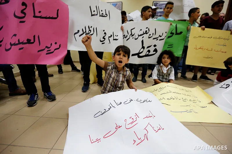 Palestinian children hold placards during a protest against the power and water crisis, at Hebron municipality, in the West Bank city of Hebron on August 9, 2017. Photo by Wisam Hashlamoun