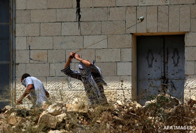 A Palestinian protester uses a slingshot to hurl stones towards Israeli security forces during clashes following a demonstration against the expropriation of Palestinian land by Israel in the village of Kfar Qaddum, near...