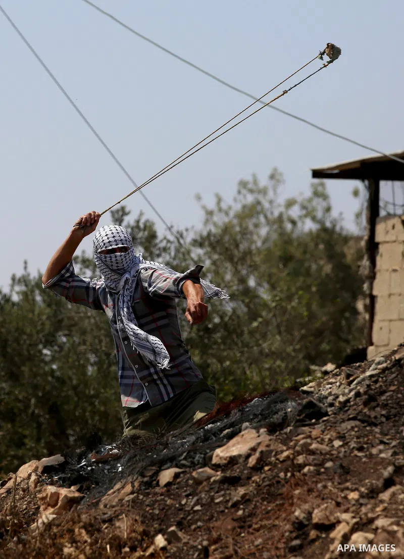 A Palestinian protester uses a slingshot to hurl stones towards Israeli security forces during clashes following a demonstration against the expropriation of Palestinian land by Israel in the village of Kfar Qaddum, near...