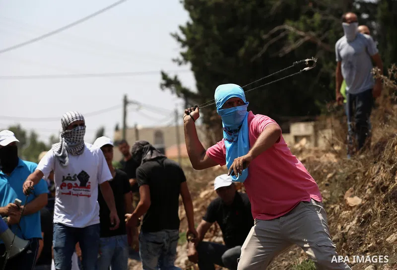 A Palestinian protester uses a slingshot to hurl stones towards Israeli security forces during clashes following a demonstration against the expropriation of Palestinian land by Israel in the village of Kfar Qaddum, near...