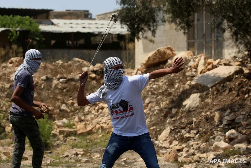A Palestinian protester uses a slingshot to hurl stones towards Israeli security forces during clashes following a demonstration against the expropriation of Palestinian land by Israel in the village of Kfar Qaddum, near...