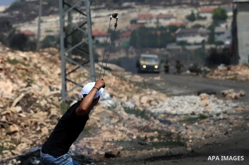 A Palestinian protester uses a slingshot to hurl stones towards Israeli security forces during clashes following a demonstration against the expropriation of Palestinian land by Israel in the village of Kfar Qaddum, near...