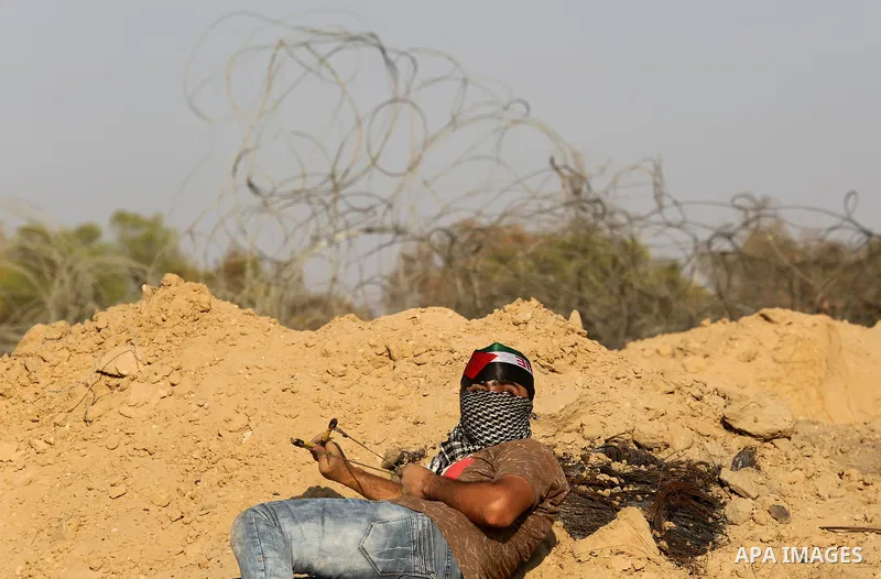 A Palestinian protester uses slingshots to hurl stones towards Israeli security forces during clashes near the border between Israel and Central Gaza Strip August 11, 2017. Photo by Ashraf Amra
