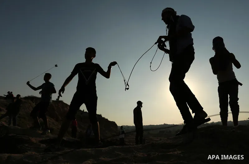 Palestinian protesters use slingshots to hurl stones towards Israeli security forces during clashes near the border between Israel and Central Gaza Strip August 11, 2017. Photo by Ashraf Amra