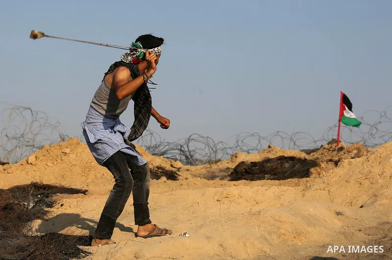 A Palestinian protester uses slingshots to hurl stones towards Israeli security forces during clashes near the border between Israel and Central Gaza Strip August 11, 2017. Photo by Ashraf Amra