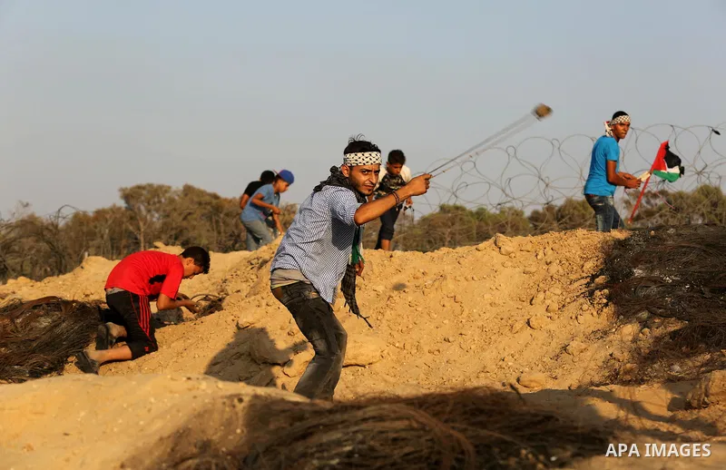 A Palestinian protester uses slingshots to hurl stones towards Israeli security forces during clashes near the border between Israel and Central Gaza Strip August 11, 2017. Photo by Ashraf Amra