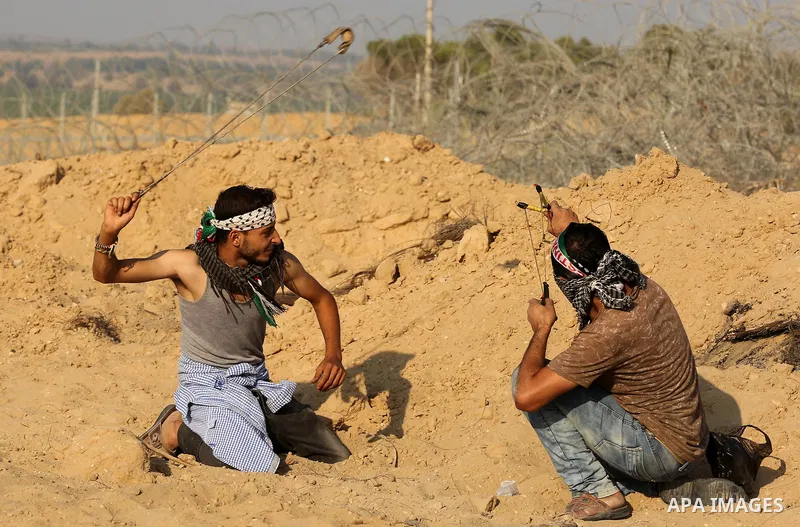 Palestinian protesters use slingshots to hurl stones towards Israeli security forces during clashes near the border between Israel and Central Gaza Strip August 11, 2017. Photo by Ashraf Amra