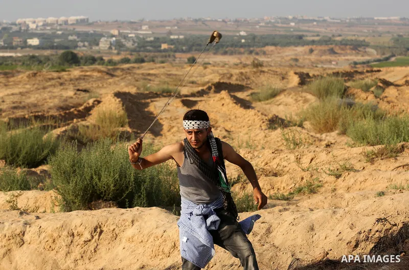 A Palestinian protester uses slingshots to hurl stones towards Israeli security forces during clashes near the border between Israel and Central Gaza Strip August 11, 2017. Photo by Ashraf Amra