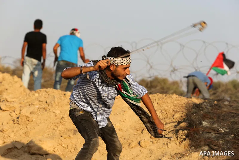 A Palestinian protester uses slingshots to hurl stones towards Israeli security forces during clashes near the border between Israel and Central Gaza Strip August 11, 2017. Photo by Ashraf Amra