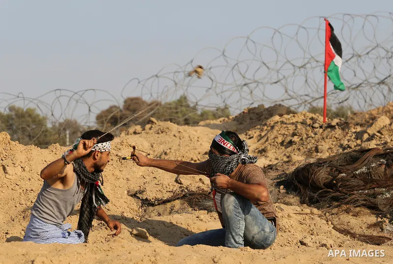 Palestinian protesters use slingshots to hurl stones towards Israeli security forces during clashes near the border between Israel and Central Gaza Strip August 11, 2017. Photo by Ashraf Amra