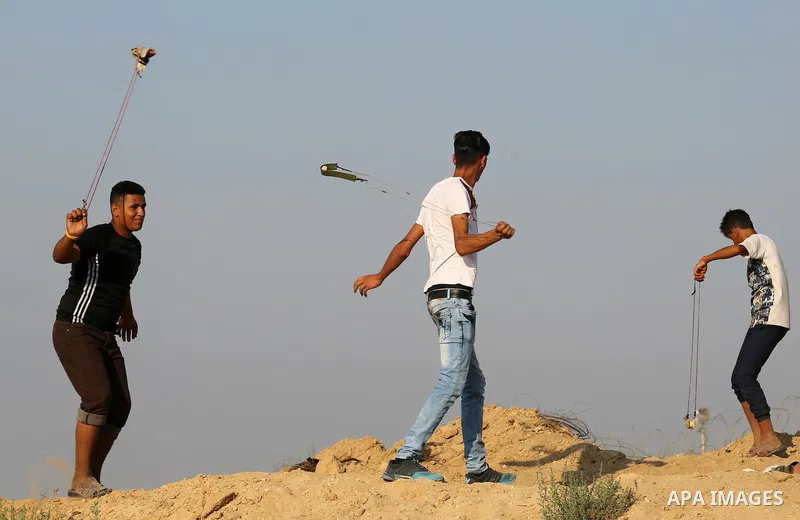 Palestinian protesters use slingshots to hurl stones towards Israeli security forces during clashes near the border between Israel and Central Gaza Strip August 11, 2017. Photo by Ashraf Amra