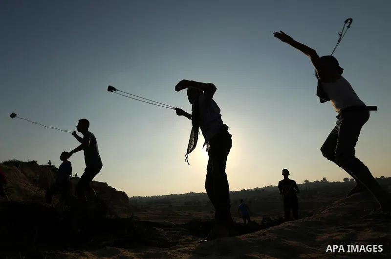 Palestinian protesters use slingshots to hurl stones towards Israeli security forces during clashes near the border between Israel and Central Gaza Strip August 11, 2017. Photo by Ashraf Amra