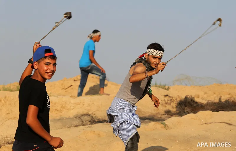 Palestinian protesters use slingshots to hurl stones towards Israeli security forces during clashes near the border between Israel and Central Gaza Strip August 11, 2017. Photo by Ashraf Amra